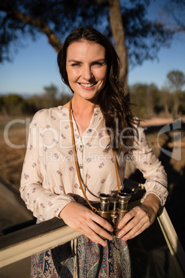 Portrait of confident woman standing with binoculars in vehicle