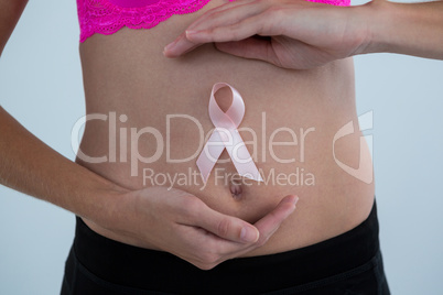 Mid section of woman with Breast Cancer Awareness ribbon on abdomen