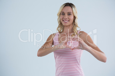 Portrait of smiling woman making heart shape on pink ribbon