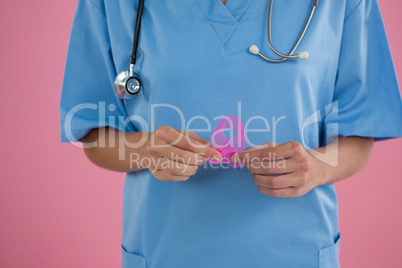 Mid section of female doctor in scrubs holding Breast Cancer Awareness ribbon
