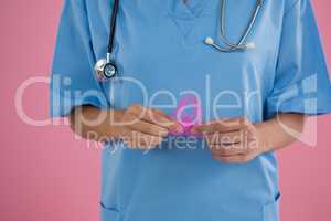 Mid section of female doctor in scrubs holding Breast Cancer Awareness ribbon