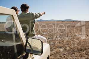 Rear view of man with woman on off road vehicle pointing at landscape