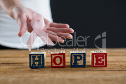 Mid section of woman showing Breast Cancer Awareness ribbon with hope text on table