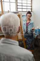Woman interacting with senior man while painting on canvas