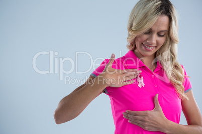 Smiling woman with pink ribbon touching on breast