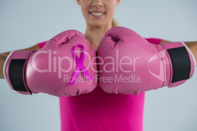 Mid section of smiling woman with boxing gloves and pink ribbon