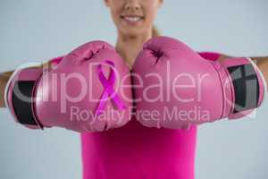 Mid section of smiling woman with boxing gloves and pink ribbon