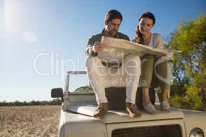 Young couple holding map on tire over off road vehicle