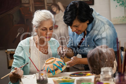 Woman assisting senior woman in painting bowl at drawing class