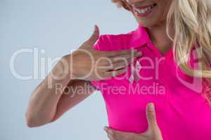 Mid section of smiling woman with pink ribbon touching on breast