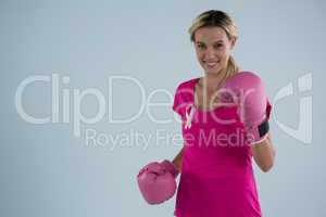 Portrait of smiling woman with boxing gloves and and pink ribbon