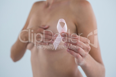 Mid section of woman covering breast while showing pink ribbon