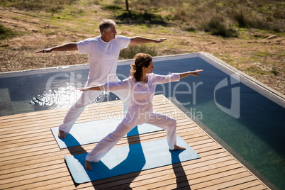 Couple practicing yoga on at poolside