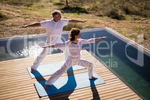 Couple practicing yoga on at poolside