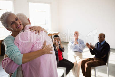 Senior friends applauding while looking at man and woman embracing