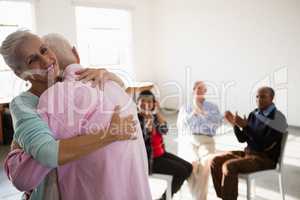 Senior friends applauding while looking at man and woman embracing