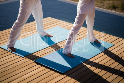 Low section of couple practicing yoga on at poolside