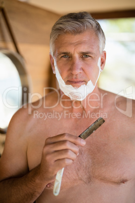 Portrait of man shaving his beard with razor in cottage
