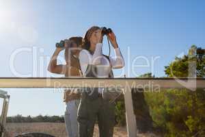 Couple looking through binoculars at forest on sunny day