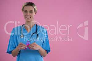 Portrait of smiling female doctor in scrubs showing Breast Cancer Awareness ribbon