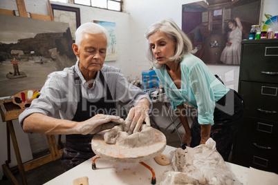 Senior woman assisting senior man in making pottery during drawing class