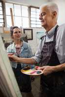 Woman interacting while senior man painting on canvas