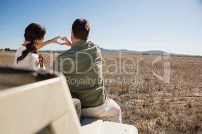 Rear view of couple making heart shape with hands on off road vehicle