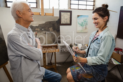 Woman interacting with senior man while sketching on canvas
