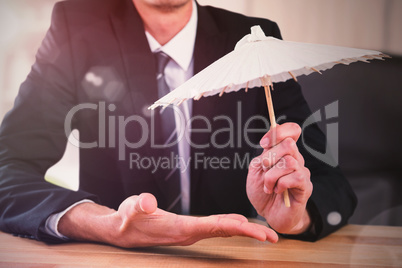 Composite image of businessman holding paper umbrella