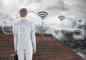 Wi-fi icons and Businessman standing on Roof with chimney and misty city
