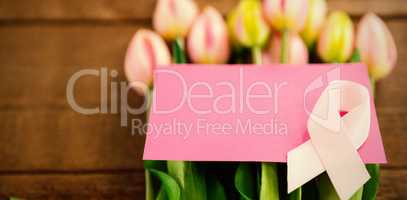 High angle view of pink Breast Cancer Awareness ribbon with blank card on fresh tulips