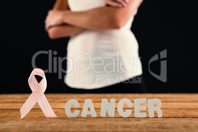 Mid section of woman by cancer text and ribbon on table