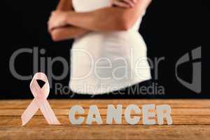 Mid section of woman by cancer text and ribbon on table