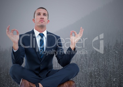 Business man meditating against trees and grey sky