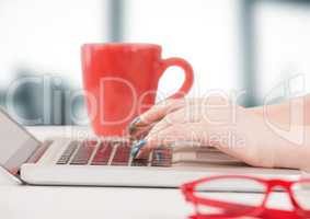 Hands with laptop and red coffee cup against blurry grey office