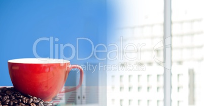 Red coffee cup on red and white table cloth with beans against blue background and blurry office tra