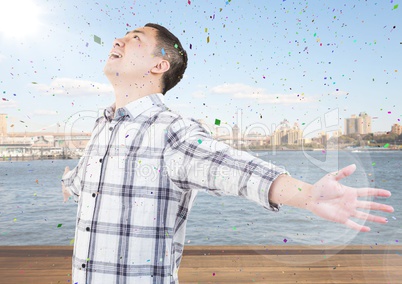 Man with arms outstretched against water and skyline with flare and confetti