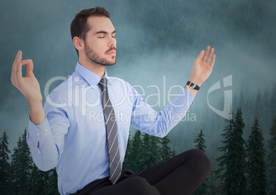 Business man meditating against foggy trees