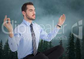 Business man meditating against foggy trees