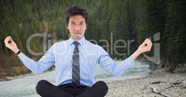 Business man meditating against river