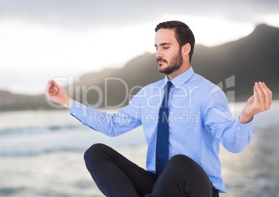 Business man meditating against blurry coastline