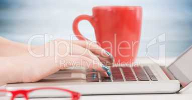 Hands with laptop and red coffee cup against blurry blue wood panel