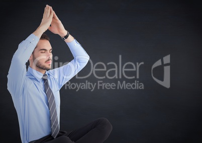 Business man meditating against navy chalkboard