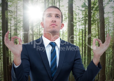 Business man meditating against blurry forest with flare