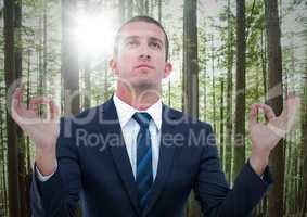 Business man meditating against blurry forest with flare