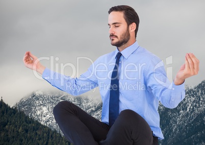 Business man meditating against mountains and grey sky