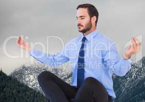 Business man meditating against mountains and grey sky
