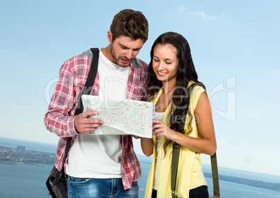 Millennial couple with map against blurry sky and coastline