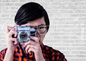 Close up of millennial man with camera against white brick wall