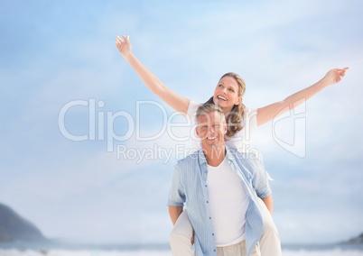 Middle aged couple piggy back against blurry sky and beach